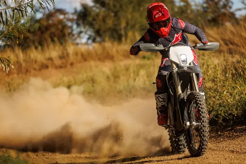An electric motocross bike kicking up dust behind it on a dirt track 
